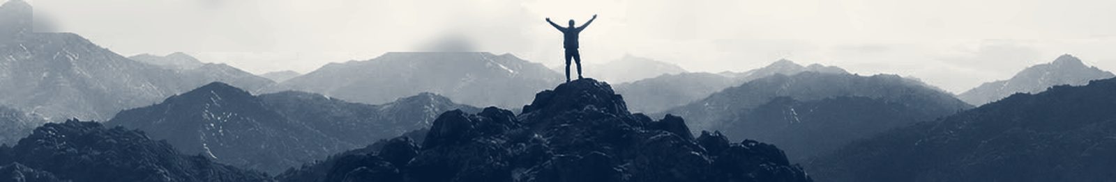 Una persona con los brazos abiertos en la cima de una montaña, entre cordilleras